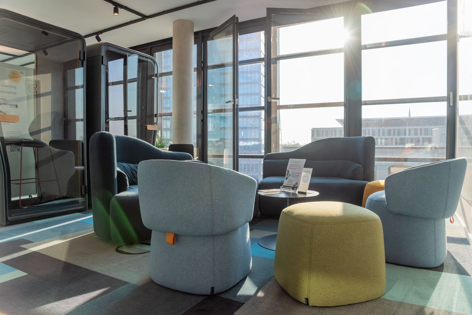 Lounge mit Sesseln und Hockern vor der Fensterfront